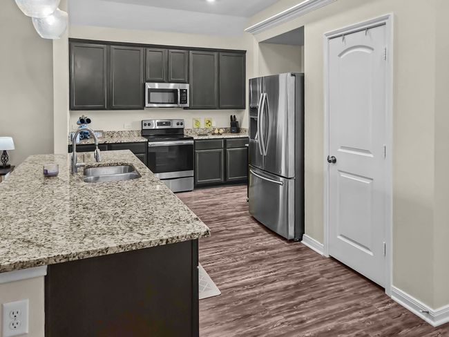 Kitchen featuring appliances with stainless steel finishes, dark wood-type flooring, light stone countertops, and dark cabinetry | Image 5