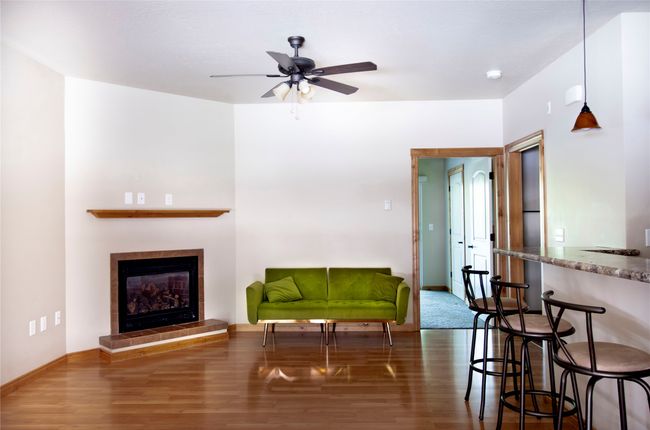 Living area with wood finished floors, a ceiling fan, and a tile fireplace | Image 8