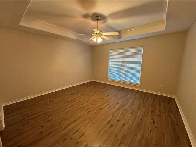 Empty room featuring a tray ceiling, ceiling fan, dark wood-type flooring, and crown molding | Image 7