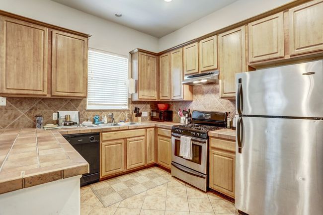 Kitchen with stainless steel appliances, under cabinet range hood, tile counters, light brown cabinets, and tasteful backsplash | Image 8