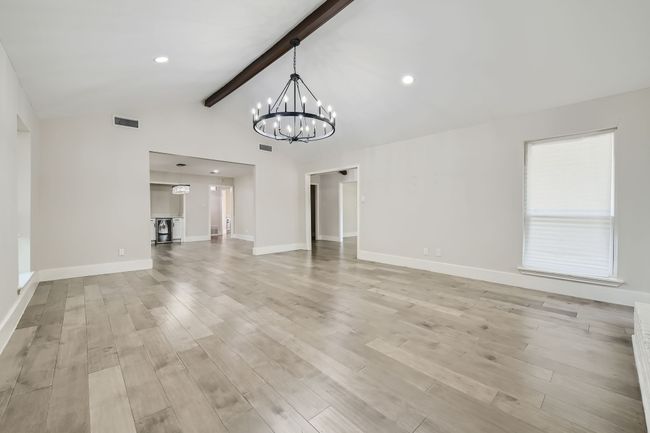 Unfurnished living room with light wood finished floors, an inviting chandelier, visible vents, and vaulted ceiling with beams | Image 6