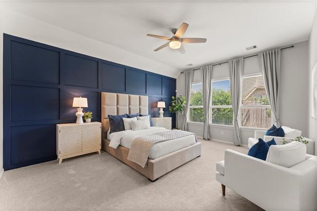 Spacious primary suite features a striking navy accent wall, large windows with backyard views, plush carpeting, and a cozy sitting area | Image 21