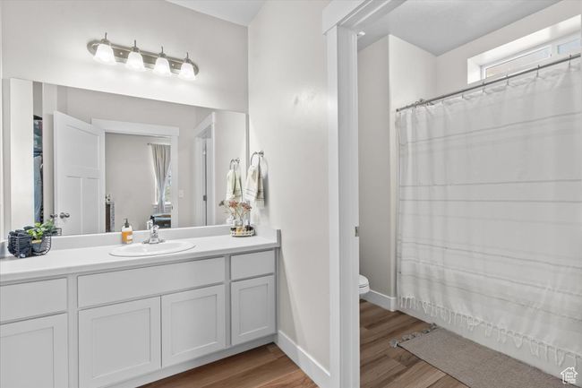 Full bathroom with vanity, wood finished floors, toilet, baseboards, and curtained shower | Image 7