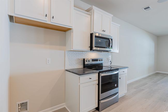 Kitchen with tasteful backsplash, visible vents, light wood-style flooring, stainless steel appliances, and white cabinetry | Image 22