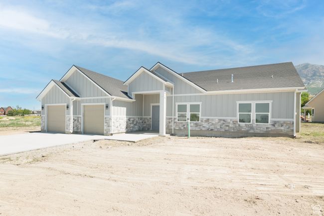 View of front of house featuring stone siding, a shingled roof, an attached garage, concrete driveway, and board and batten siding | Image 24
