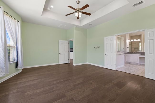Unfurnished bedroom featuring a tray ceiling, multiple windows, wood finished floors, ensuite bathroom, and recessed lighting | Image 14