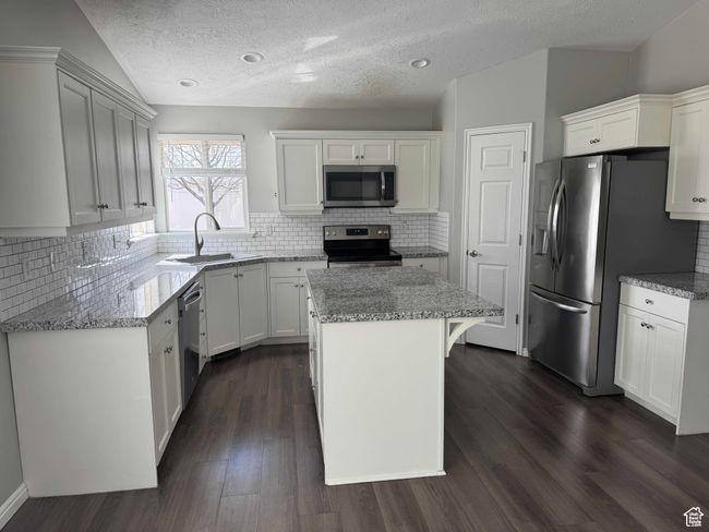 Kitchen featuring stainless steel appliances, a sink, a center island, light stone countertops, and a textured ceiling | Image 8