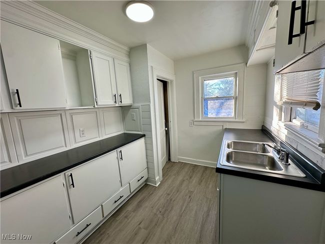 Kitchen featuring dark countertops, wood finished floors, a sink, baseboards, and white cabinetry | Image 7