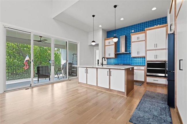 Kitchen featuring wall chimney exhaust hood, french doors, light wood finished floors, black appliances, and light countertops | Image 12