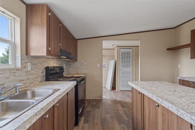 Kitchen with black range with electric stovetop, light countertops, under cabinet range hood, and dark vinyl floors | Image 14