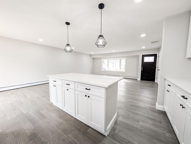 Kitchen with white cabinetry, a baseboard heating unit, light countertops, and wood finished floors | Image 7