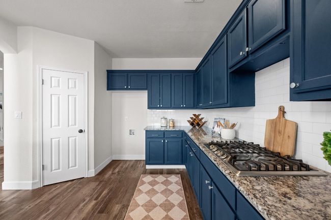 Kitchen with stainless steel gas stovetop, blue cabinets, dark wood-type flooring, baseboards, and backsplash | Image 10