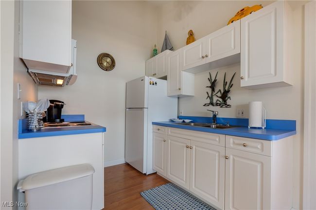 Kitchen with freestanding refrigerator, light wood-style flooring, white cabinets, and dark countertops | Image 10