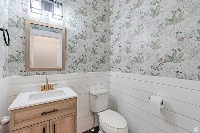 Half bathroom with wallpapered walls, a wainscoted wall, toilet, and vanity | Image 9