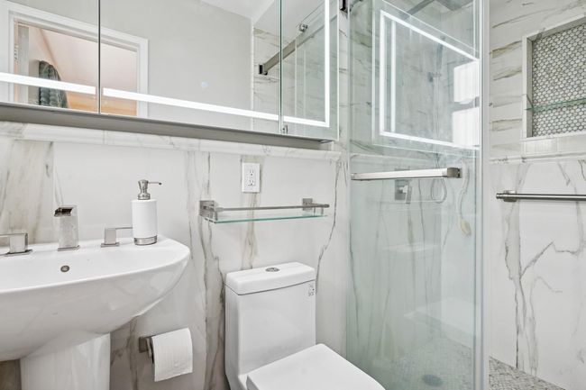 Full bathroom featuring a marble finish shower, toilet, and a sink | Image 13