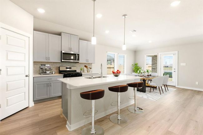 A chef’s dream! This stunning kitchen features high ceilings, large windows, elegant pebble cabinets, Quartz countertops, and a sleek tile backsplash. Stainless steel appliances, recessed and custom pendant lighting add style, while the oversized Quartz island with a double sink and breakfast bar offers the perfect gathering space. With extended counter space and a walk-in pantry, this kitchen seamlessly flows into the spacious family room—perfect for entertaining! | Image 6