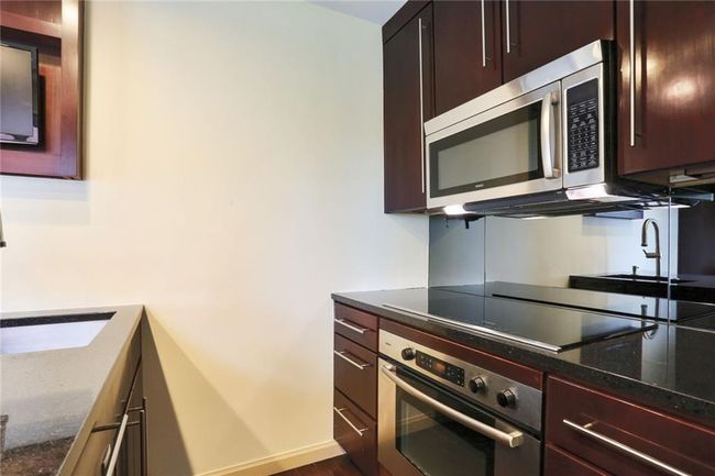 Kitchen with dark stone countertops, stained cabinets, and Bosch appliances with stainless steel finishes | Image 6