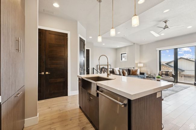 Kitchen featuring stainless steel dishwasher, open floor plan, light countertops, an island with sink, and light wood finished floors | Image 10