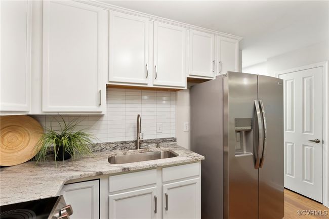 Kitchen featuring appliances with stainless steel finishes, white cabinetry, backsplash, light stone counters, and light wood-style flooring | Image 8