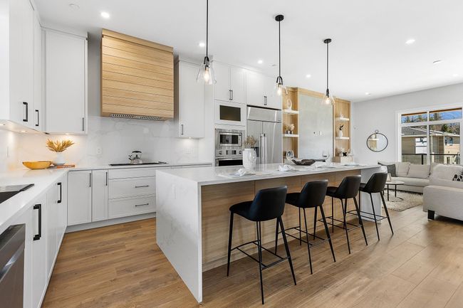 Kitchen with appliances with stainless steel finishes, range hood, a breakfast bar area, backsplash, and light wood-type flooring | Image 4