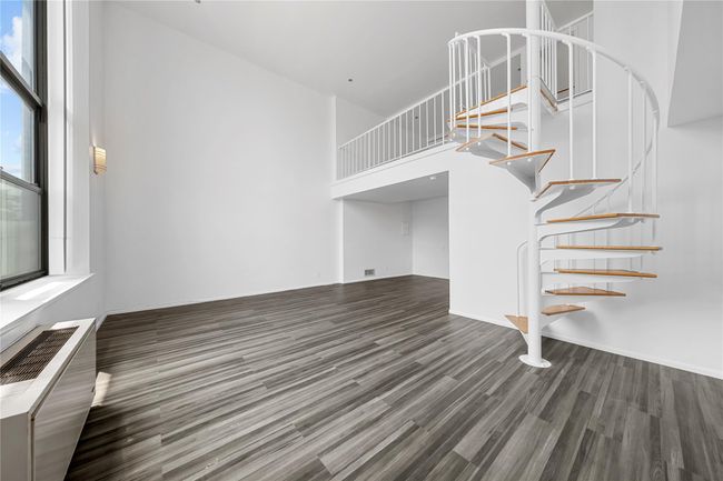 Unfurnished living room featuring stairway, wood finished floors, a towering ceiling, and a wall mounted AC | Image 13