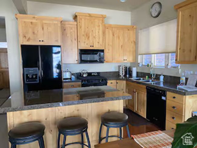 Kitchen with a sink, black appliances, a kitchen bar, and light brown cabinets | Image 7