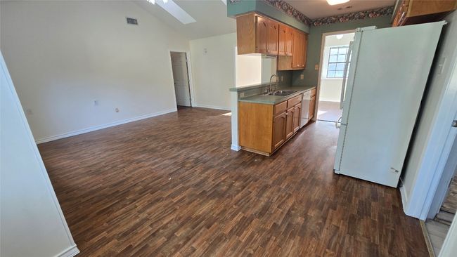 Kitchen featuring freestanding refrigerator, a skylight, dark wood-style flooring, dishwasher, and high vaulted ceiling | Image 12