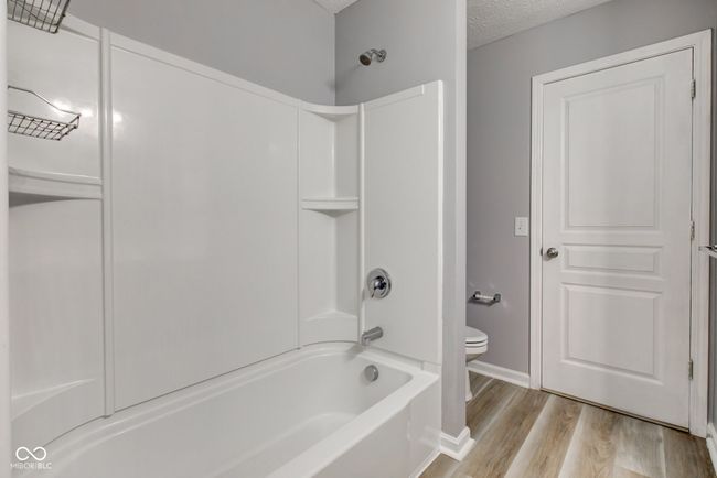 bathroom with wood finished floors, shower / washtub combination, and a textured ceiling | Image 42