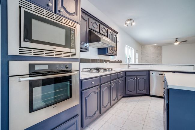 Kitchen featuring stainless steel appliances, light countertops, under cabinet range hood, ceiling fan, and a peninsula | Image 12