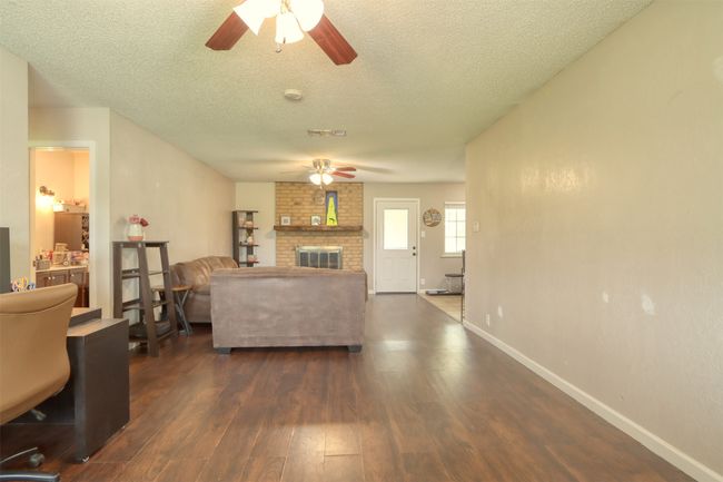Living area with ceiling fan, dark wood-style floors, a textured ceiling, and a brick fireplace | Image 9
