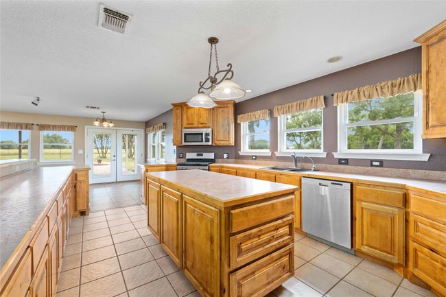 Kitchen featuring stainless steel appliances, a kitchen island, light countertops, light tile patterned floors, and a textured ceiling | Image 4