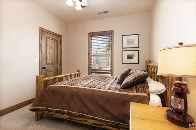 Carpeted bedroom featuring baseboards, visible vents, an inviting chandelier, and a textured ceiling | Image 37