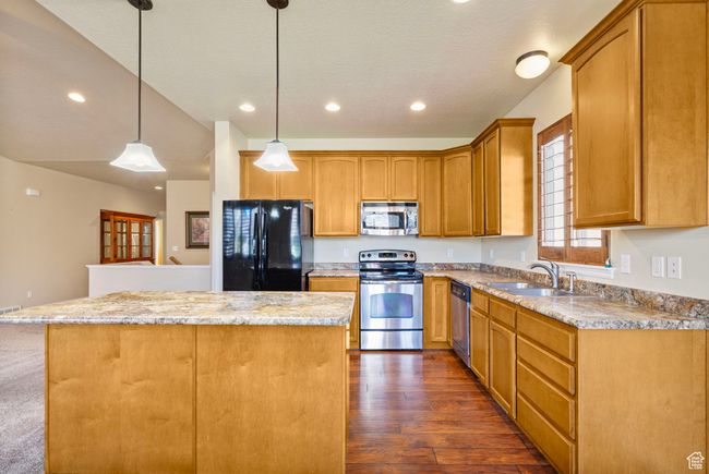 Kitchen featuring a sink, a center island, hanging light fixtures, stainless steel appliances, and dark wood-type flooring | Image 6