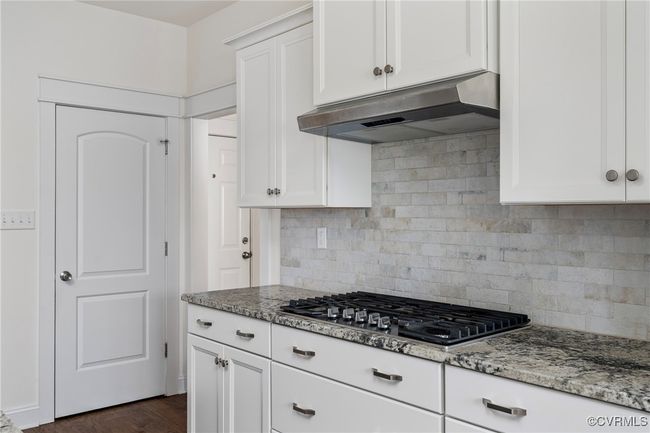 Kitchen with light stone counters, white cabinets, stainless steel gas cooktop, under cabinet range hood, and backsplash | Image 12