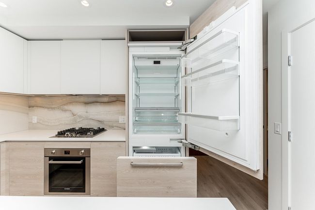 Kitchen with dark wood-style floors, light countertops, white cabinetry, backsplash, and stainless steel appliances | Image 12