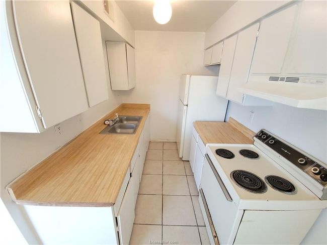Kitchen with light tile patterned flooring, sink, white cabinets, and white appliances | Image 25