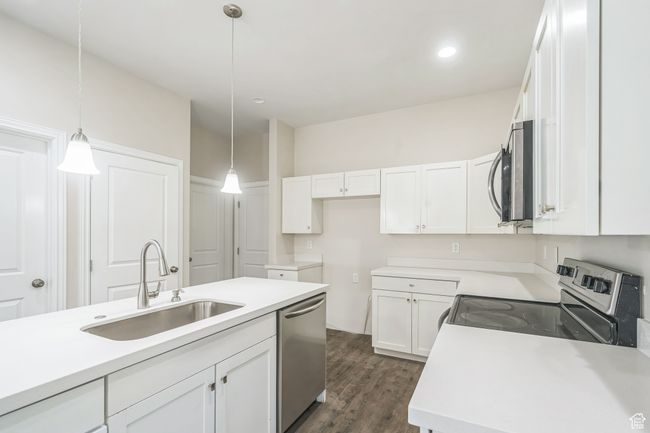 Kitchen with stainless steel appliances, white cabinetry, pendant lighting, dark wood-style floors, and light countertops | Image 11