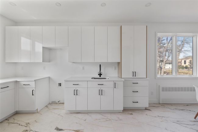 Kitchen featuring white cabinets, a sink, radiator heating unit, marble finish floor, and light countertops | Image 11