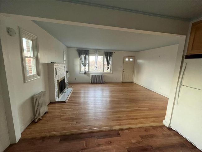 Unfurnished living room featuring radiator heating unit, wood-type flooring, and a healthy amount of sunlight | Image 4
