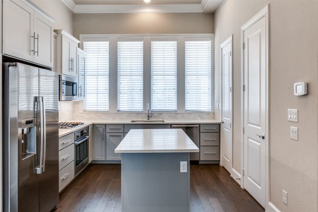 Kitchen featuring appliances with stainless steel finishes, a kitchen island, dark wood finished floors, ornamental molding, and light countertops | Image 17