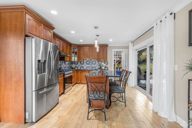 Kitchen with appliances with stainless steel finishes, under cabinet range hood, glass insert cabinets, light wood finished floors, and a kitchen breakfast bar | Image 14