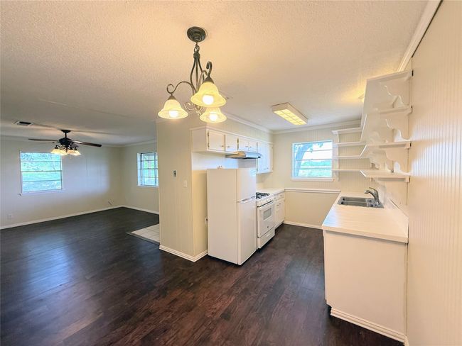 Kitchen featuring white appliances, open shelves, light countertops, a textured ceiling, and dark wood-type flooring | Image 6