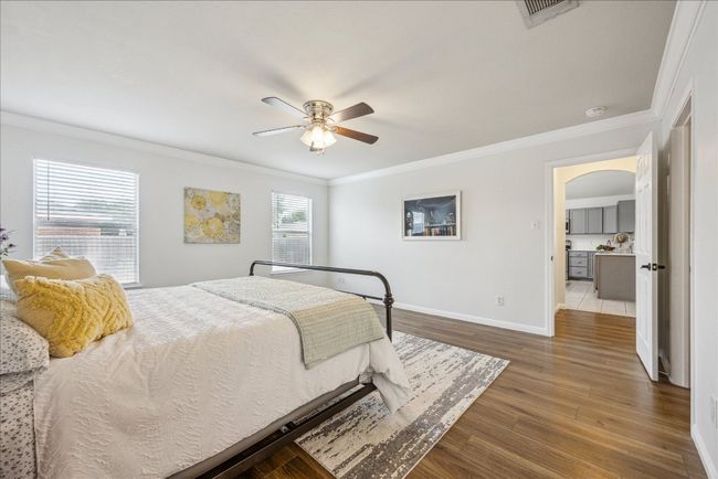 Primary bedroom featuring crown molding and arched walkways, vinyl flooring, large windows allowing natural light from the yard, and a ceiling fan | Image 15