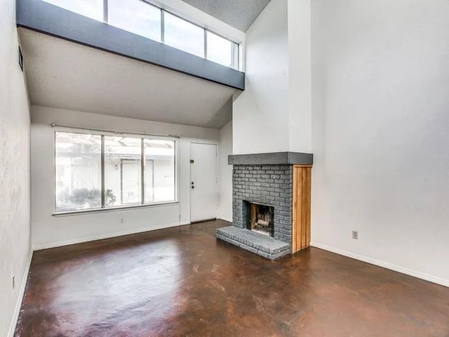 Unfurnished living room featuring concrete floors, a brick fireplace, and a towering ceiling | Image 4