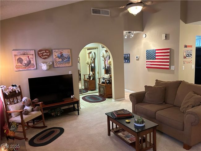 Living area with a ceiling fan, arched walkways, light colored carpet, a high ceiling, and light tile patterned flooring | Image 9