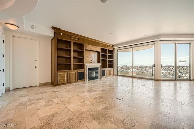 Unfurnished living room featuring stone tile floors, built in features, a glass covered fireplace, and baseboards | Image 7