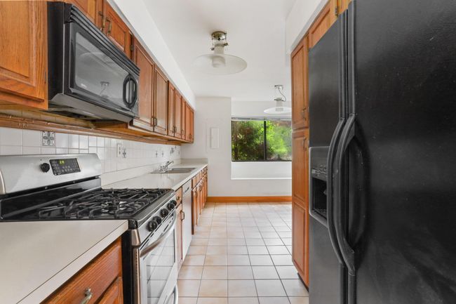 Kitchen featuring black appliances, brown cabinetry, a sink, light tile patterned floors, and light countertops | Image 8