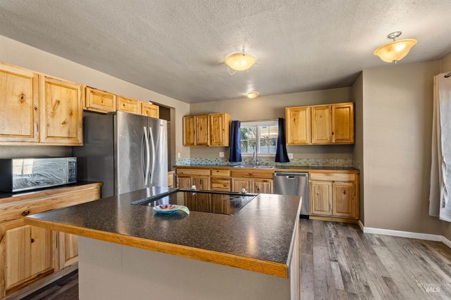 Kitchen featuring a textured ceiling, dark wood-type flooring, black appliances, dark countertops, and a center island | Image 13