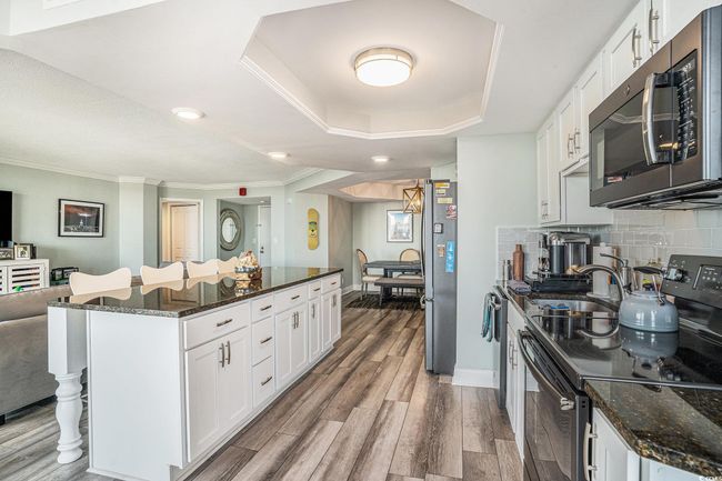 Kitchen featuring black appliances, wood finished floors, white cabinets, dark stone counters, and a kitchen bar | Image 13