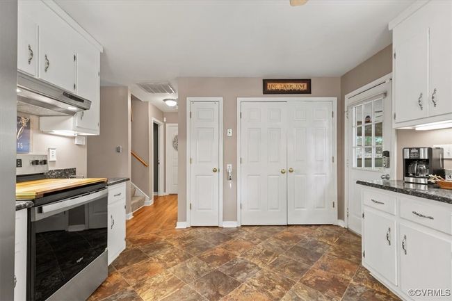 Kitchen with stainless steel electric range oven, under cabinet range hood, dark countertops, white cabinetry, and baseboards | Image 17